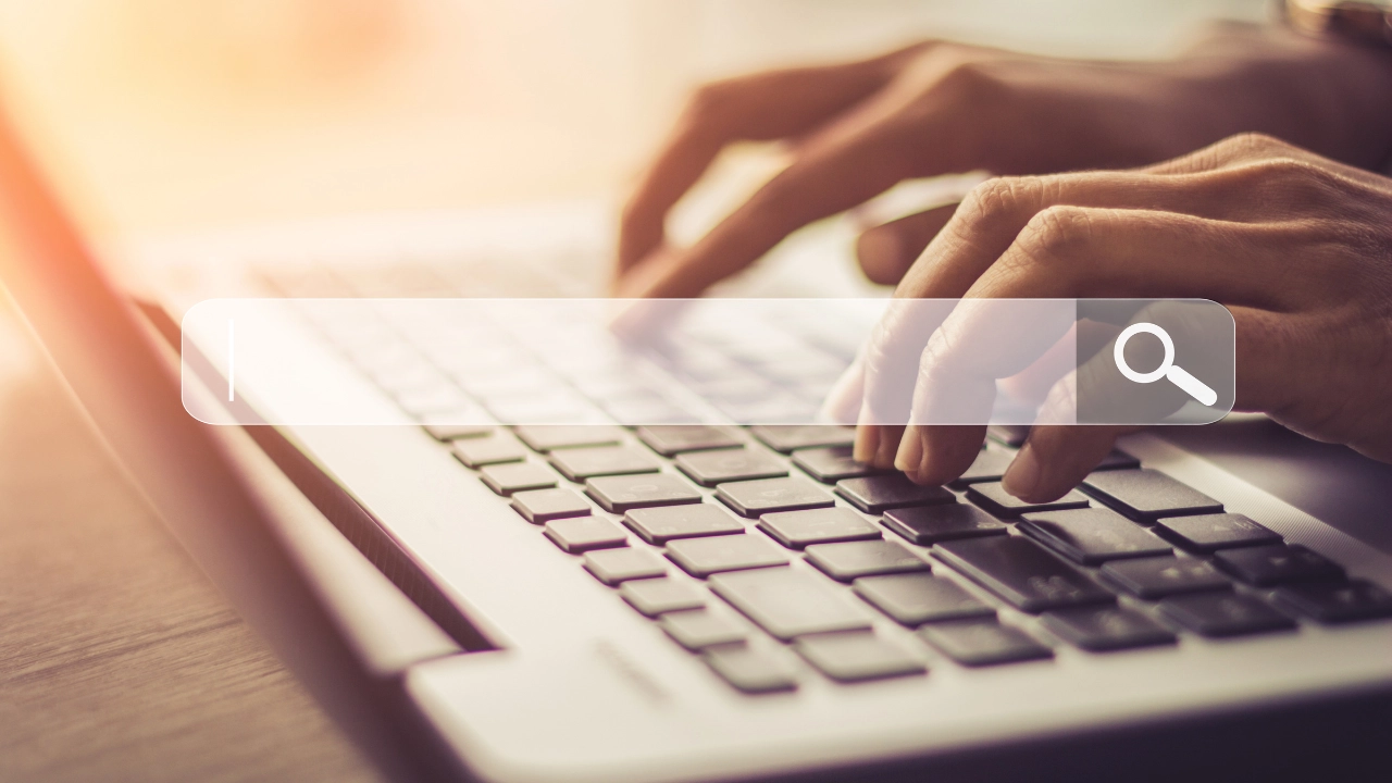 Mains sur le clavier d'un ordinateur portable avec une barre de recherche, pour recruter sur LinkedIn